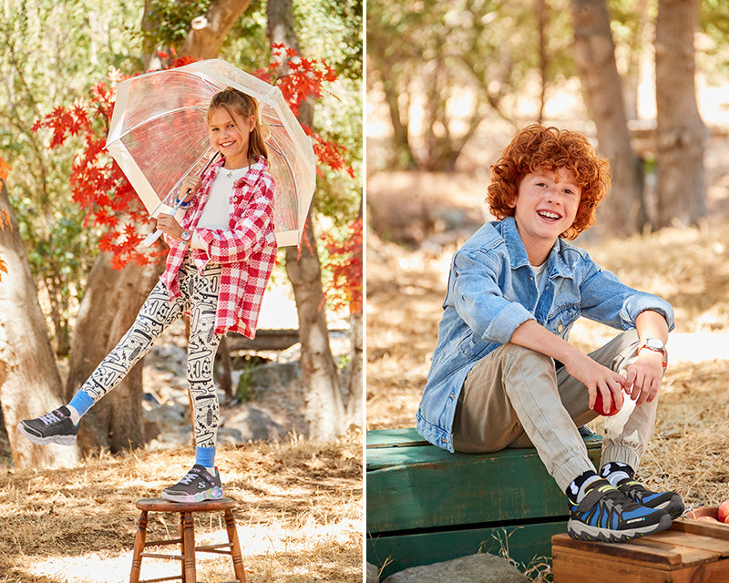 Smilende pige med en paraply iført Skechers blinkesko og en smilende dreng, som sidder på en grøn æske med Skechers vandtætte sko til børn 
